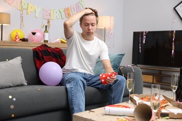 Man suffering from hangover on sofa in messy room after party