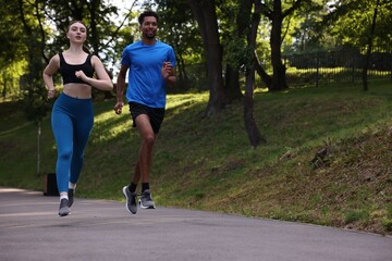 Obraz premium Couple in sportswear running in park, low angle view. Space for text