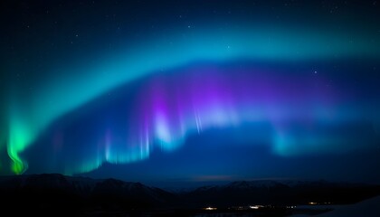 Vibrant green, blue, and purple Aurora Borealis illuminating the dark night sky over a snowy landscape with distant lights.