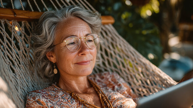 cheerful retired woman enjoying garden relaxation lying in hammock using tablet and browsing internet in daylight symbolizing joyful modern senior lifestyle