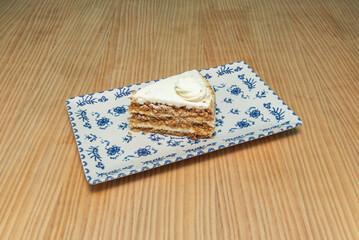 A slice of carrot cake with toasted walnuts, cheesecake frosting, and spices, topped with a candied carrot garnish