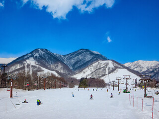 Winter landscape from the base of a ski slope with a view of snowy mountains and visitors (Tsugaike Kogen, Hakuba, Nagano, Japan)