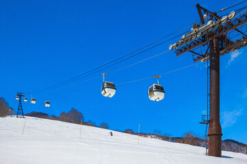 Gondola lifts going up a snowy slope under a clear blue sky (Tsugaike Kogen, Hakuba, Nagano, Japan)