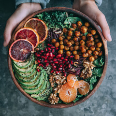 Colorful Buddha bowl with avocado, roasted chickpeas, pomegranate, citrus, walnuts, and greens, served in a wooden bowl for a healthy vegan meal.