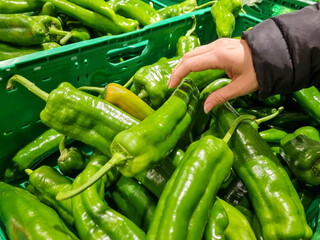 A woman buying while piping, a hand picking a green pepper