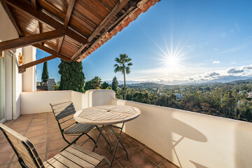 an image of a luxury balcony with wooden chairs and table and sunset landscape views over the...