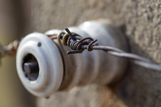 Rusty vintage porcelain electrical insulator with twisted metal wires on concrete wall.