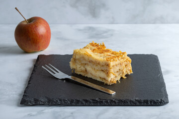 Moist layered apple semolina pie with crispy golden topping, an apple and fork.
