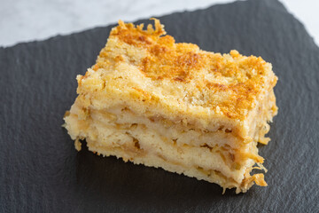 Moist layered apple semolina pie with crispy golden topping on black slate.