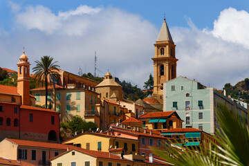 A view of a beautiful Italian old town Vintimille rising up into the hillside towards mountains in the distance. There are painted houses and church spire and wooded hills. © kovalenkovpetr