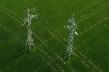 High voltage electricity transmission towers aerial view, steel power pylons standing on green agricultural field landscape, energy infrastructure grid system, renewable power distribution lines persp
