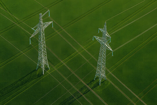 High voltage electricity transmission towers aerial view, steel power pylons standing on green agricultural field landscape, energy infrastructure grid system, renewable power distribution lines persp - Powered by Adobe