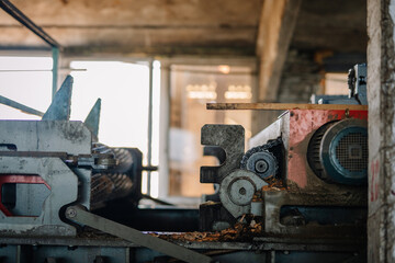 Close-up of a heavy-duty industrial woodworking machine with gears, chains, and wood shavings, used in timber processing inside a factory.