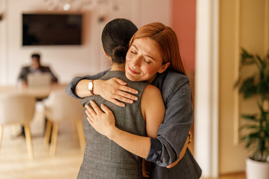 Female manager embracing coworker offering motivation and strong team connection in corporate office