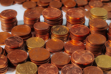 Neatly stacked euro cent coins in copper and gold tones, including 1, 2, 5, 10, and 20 cent denominations, arranged on a white surface under direct light.