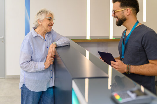 Young eye doctor talking with smiling elderly woman at reception desk during visit to ophthalmology clinic - Powered by Adobe