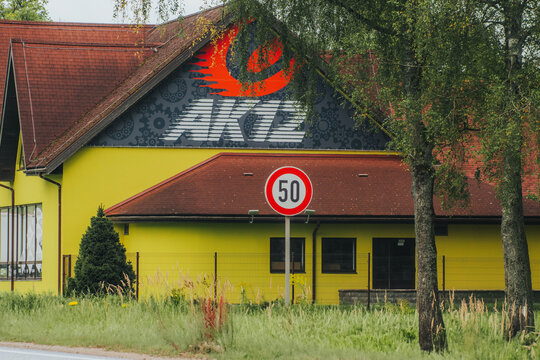 A round 50 km h speed limit sign stands in front of a bright yellow industrial building with a red roof and a large .