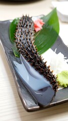 Spiny sea cucumber on dark plate with garnish