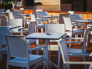 Empty outdoor restaurant terrace with white wicker chairs and tables, Cyprus