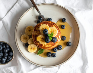 Banana Pancakes with Blueberries and Maple Syrup on Ceramic Plate