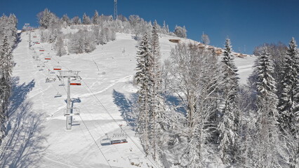 Chairlift transporting skiers uphill on snowy mountain slope, surrounded by snow covered trees and...