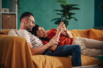 Happy couple relaxing on sofa browsing smartphone at home