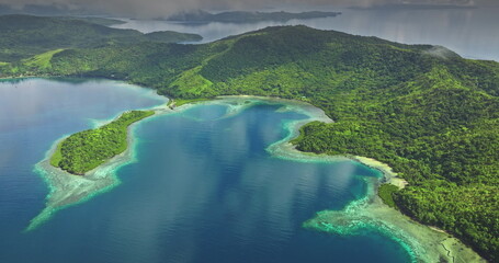Fiji islands: Aerial view of tropical islands with lush green vegetation reflecting on the turquoise ocean water under a cloudy sky. Wild nature travel landscape. Drone flight
