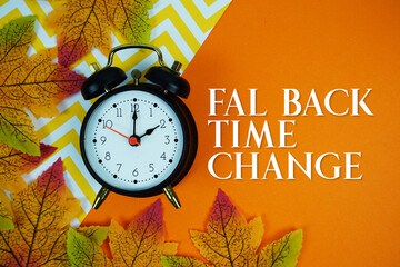 Fall Back Time Change with alarm clock and maple leaf decorated on orange background