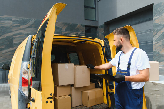 Courier checking cardboard boxes in delivery van holding clipboard