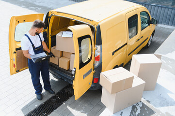 Courier checking cardboard boxes on laptop near delivery van © Serhii