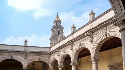 Obraz premium A large building with a tall tower and arched walkways. The arched walkways are made of stone. The sky is clear. mexico city