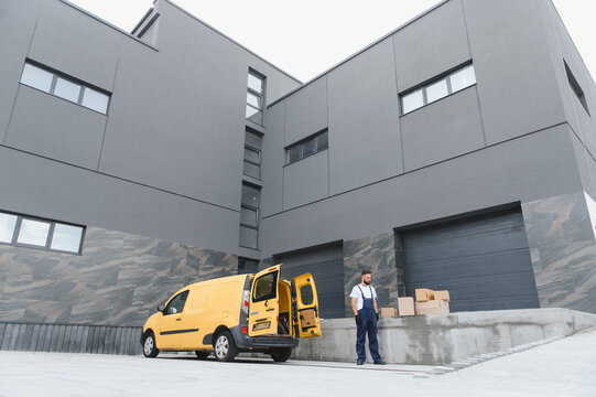 Delivery driver waiting with cardboard boxes by his van outside warehouse - Powered by Adobe