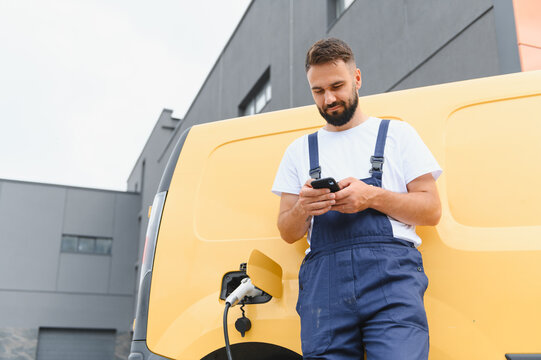 Courier using smartphone while charging electric van - Powered by Adobe