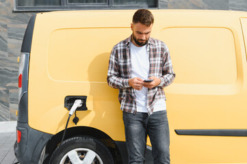 Deliveryman using smartphone while charging electric van