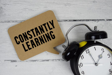 Constantly Learning text with alarm clock on wooden background