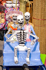 Fototapeta premium A skeleton is sitting on a blue bench with two other skeletons. The bench is decorated with skulls and bones. Day of the Dead celebration in Mexico, papel picado crafts, offerings, La Catrina