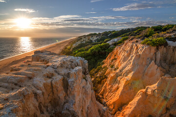 Scenic sunset over cliffs, pine forest, and golden beach in Mazagon, Huelva, Spain. Tranquil seascape ideal for travel, nature, and landscape concepts.