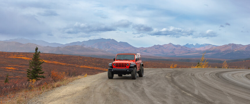 Driving orange 4x4 Jeep wrangler on rugged Denali National park road in autumn time in Alaska.