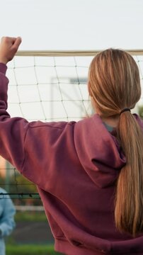 Back view of lady in maroon sweater posing in victory on outdoor volleyball court, opponent watching as one holds volleyball, showcasing moment of triumph and confidence