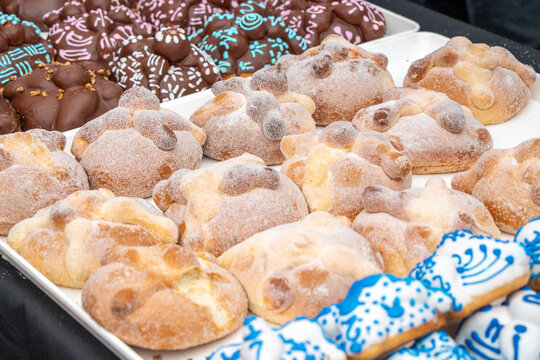 A tray of assorted pastries, including some with blue icing. The pastries are arranged in a row. Day of the Dead celebration in Mexico, papel picado crafts, offerings, La Catrina - Powered by Adobe