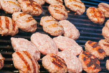 Traditional grilled meat patties cooking on hot barbecue grill with smoke and fire marks during summer picnic