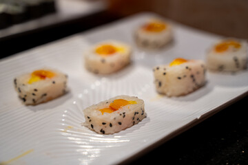 Close up of fruit sushi rolls with mango filling and sesame seeds on white plate.