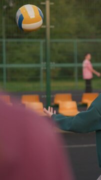 Close-up back view of instructor directing volleyball player how to serve, with other people walking outside the court in background, coaching in action on outdoor sports court