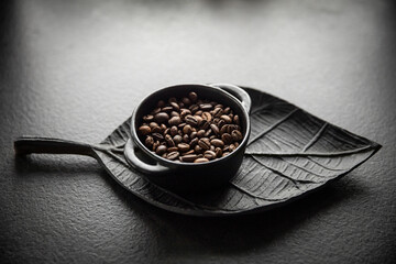 Ziarna kawy w miseczce na tle ozdobnej tacy w kształcie liścia Coffee beans in a bowl on a decorative leaf-shaped tray