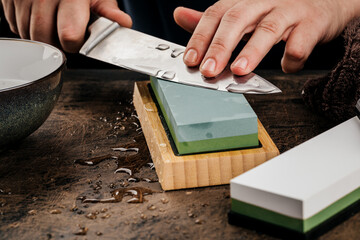 A man sharpens a knife with a grindstone on a rustic wooden table.