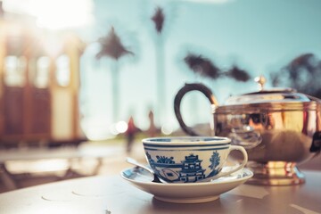 A cup of tea sits on a table, a teapot beside it, as a cable car passes in the background during a sunny afternoon in San Francisco, California