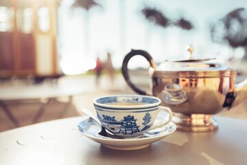 A cup of tea sits on a saucer with a spoon, next to a teapot. They sit on a table at a cafe in Santa Teresa, Rio de Janeiro, near the tram stop