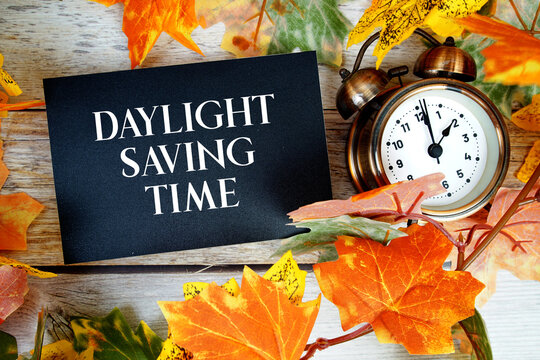 Daylight Saving Time text with alarm clock and meple leaf decoration on wooden background
