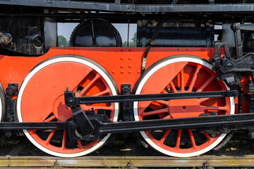Red and black wheels of an old steam locomotive standing on rails