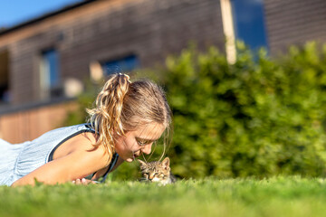 Young cheerful smiling girl playing with domestic kitten. Woman on farm rejoicing at birth of pet. Child playing with cat in yard of family house or park
